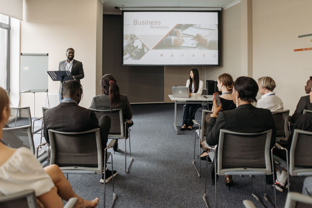 An Indian woman presenting a Mental Wellness training session to a full room of colleagues, with an agenda covering stress, resilience and workplace wellbeing